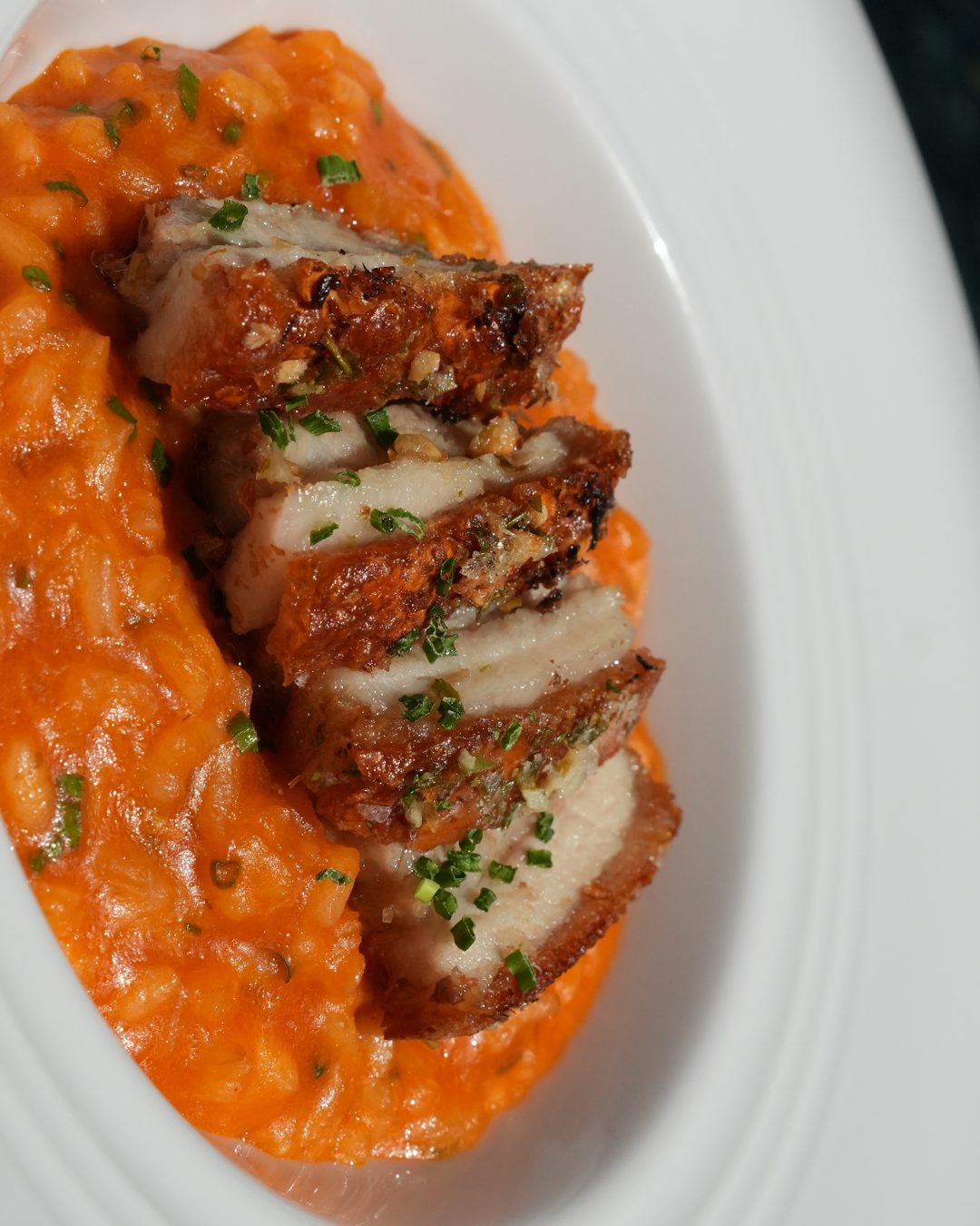 Prato do GIO com carne fatiada sobre risotto cremoso, luz natural